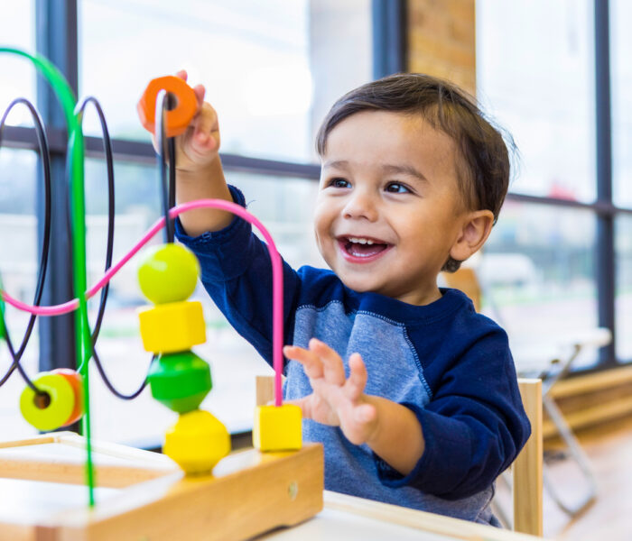 Toddler boy enjoys playing with toys in waiting room An adorable toddler boy sits at a table in a doctor's waiting room and reaches up cheerfully to play with a toy bead maze.